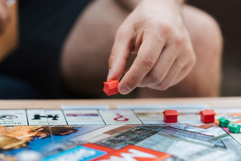 Persoon plaatst een rood Monopoly-huisje op het speelbord tijdens een spelletje Monopoly